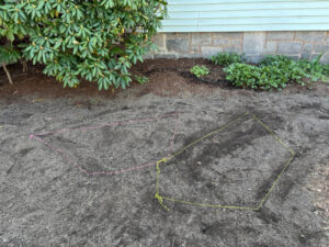 A patch of bare dirt where lawn has been removed has been divided into patches by strings, which traces a perimeter around where plants should go.